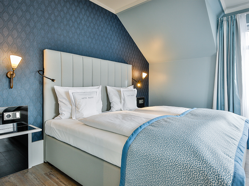 Modernes Hotelzimmer mit einem Doppelbett, blauen Akzenten, Wandlampen und einer gemusterten blauen Wand.