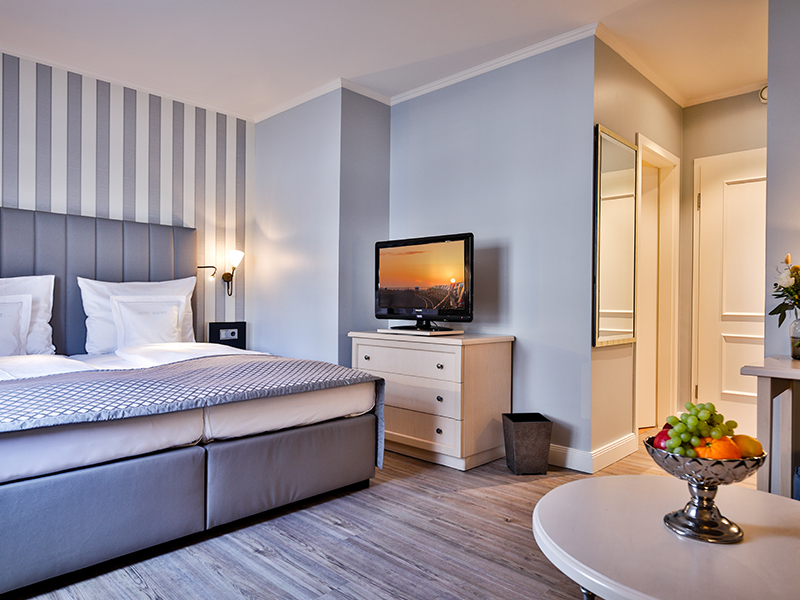 Modernes Hotelzimmer mit einem Doppelbett, Flachbildfernseher, gestreifter Wand und einer Obstschale auf dem Tisch.
