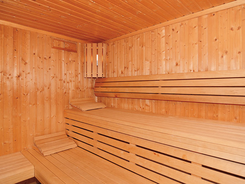 Holzgetäfelte Sauna mit Stufenbänken und hölzernen Kopfstützen, alles leer und hell erleuchtet.