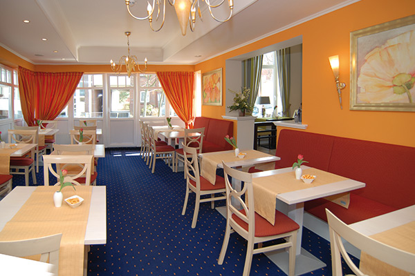 Heller, gemütlicher Speisesaal mit orangefarbenen Wänden, roten Sitzgelegenheiten, kleinen Tischen und großen Fenstern mit orangefarbenen Vorhängen.